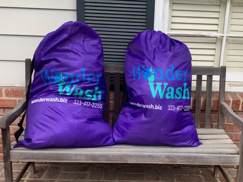 Two purple WonderWash laundry bags on a porch bench, ready for pickup